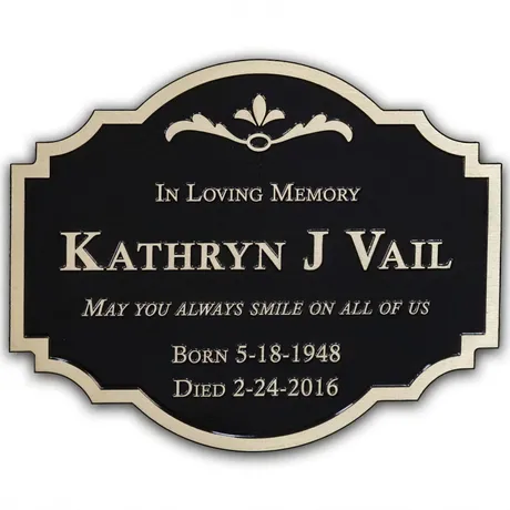 Shaped bronze memorial plaque reading In Loving Memory with raised lettering, name, dates, and a decorative border on a black background